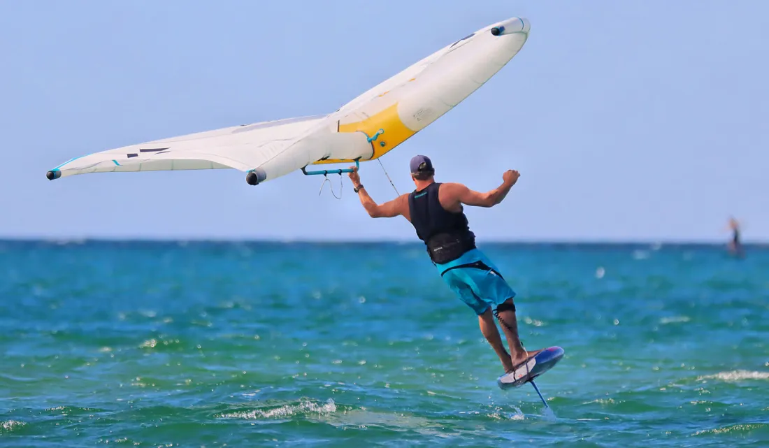 Un wing foileur tient une wing avec un boom au-dessus de la tête en tournant.