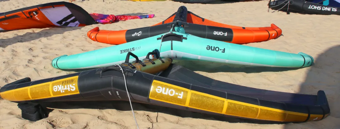 Trois wings F-One posées sur la plage.